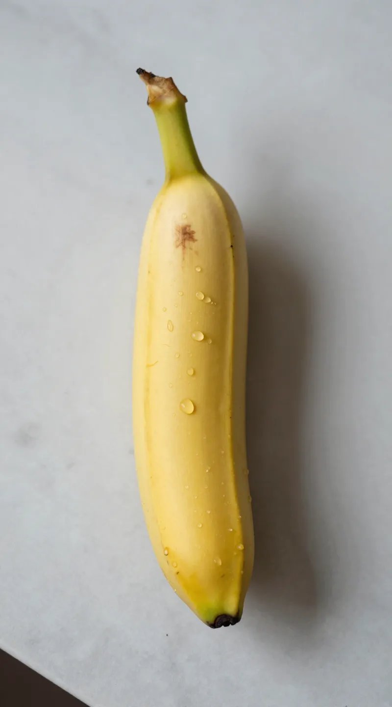 single ripe banana on marble countertop, water droplets