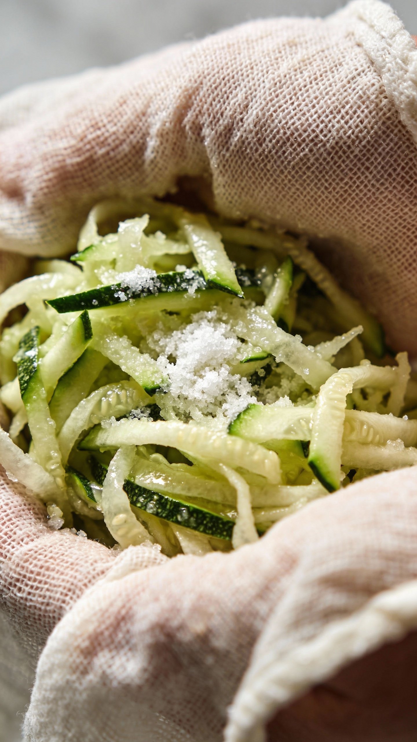 salted shredded zucchini being squeezed in cheesecloth, macro