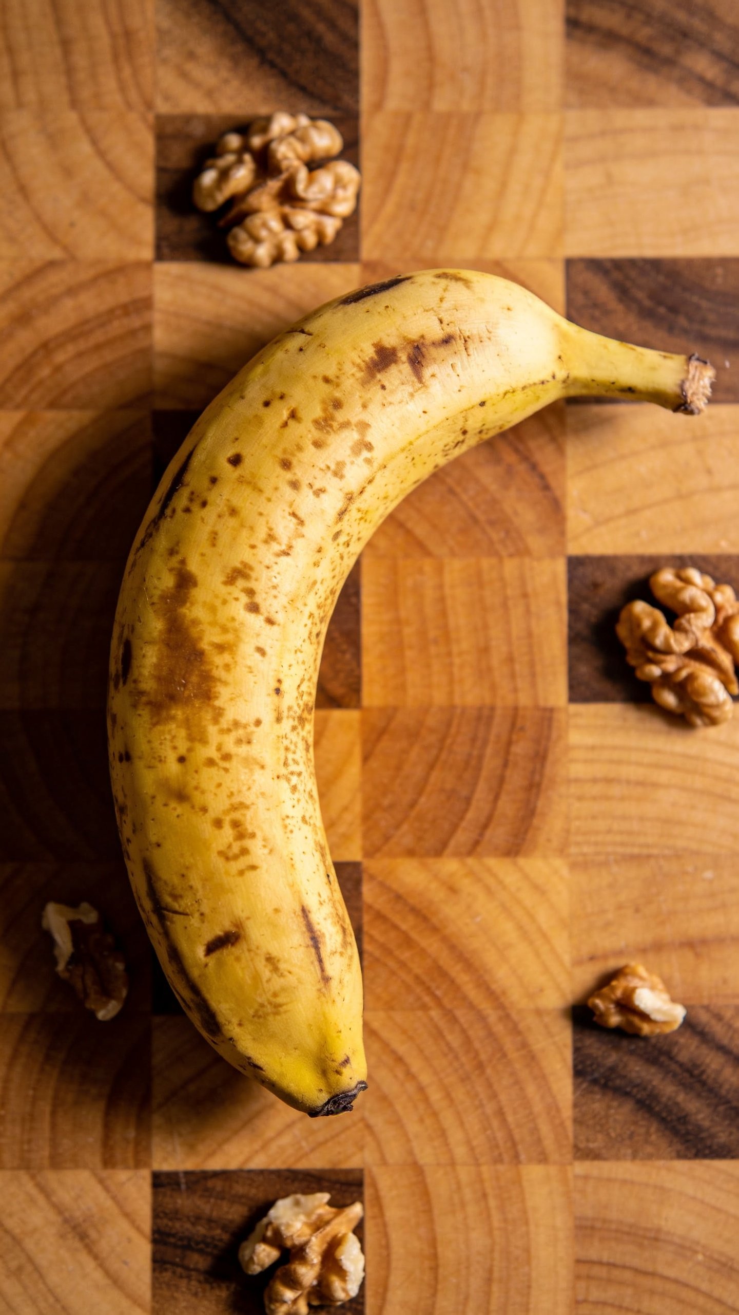 single ripe banana on walnut-studded cutting board, overhead