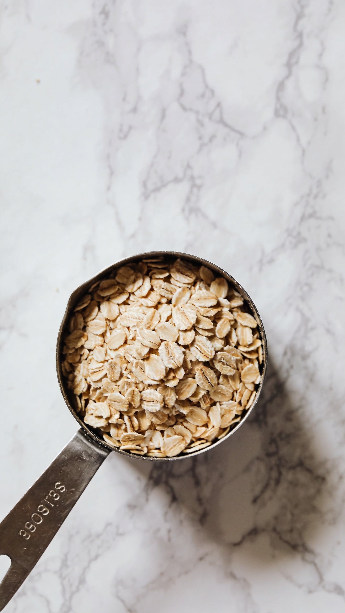 overhead shot of rolled oats measuring cup on marble surface