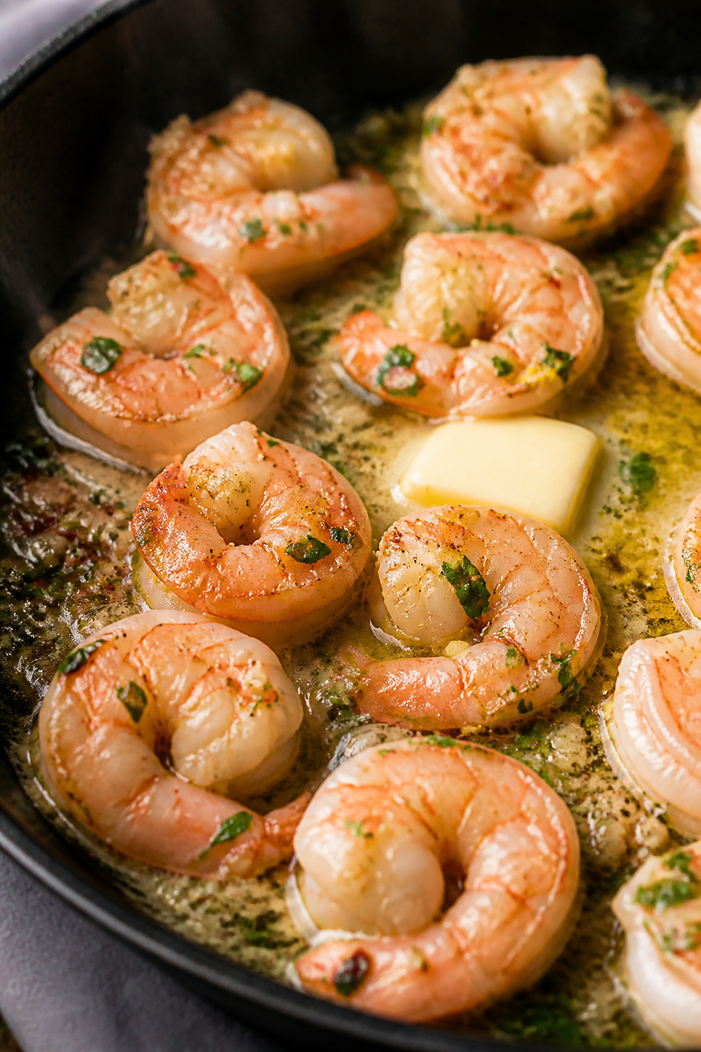 Close-up detail: Sautéed shrimp scampi in a skillet mid-cook, shrimp just turned pink and opaque, g