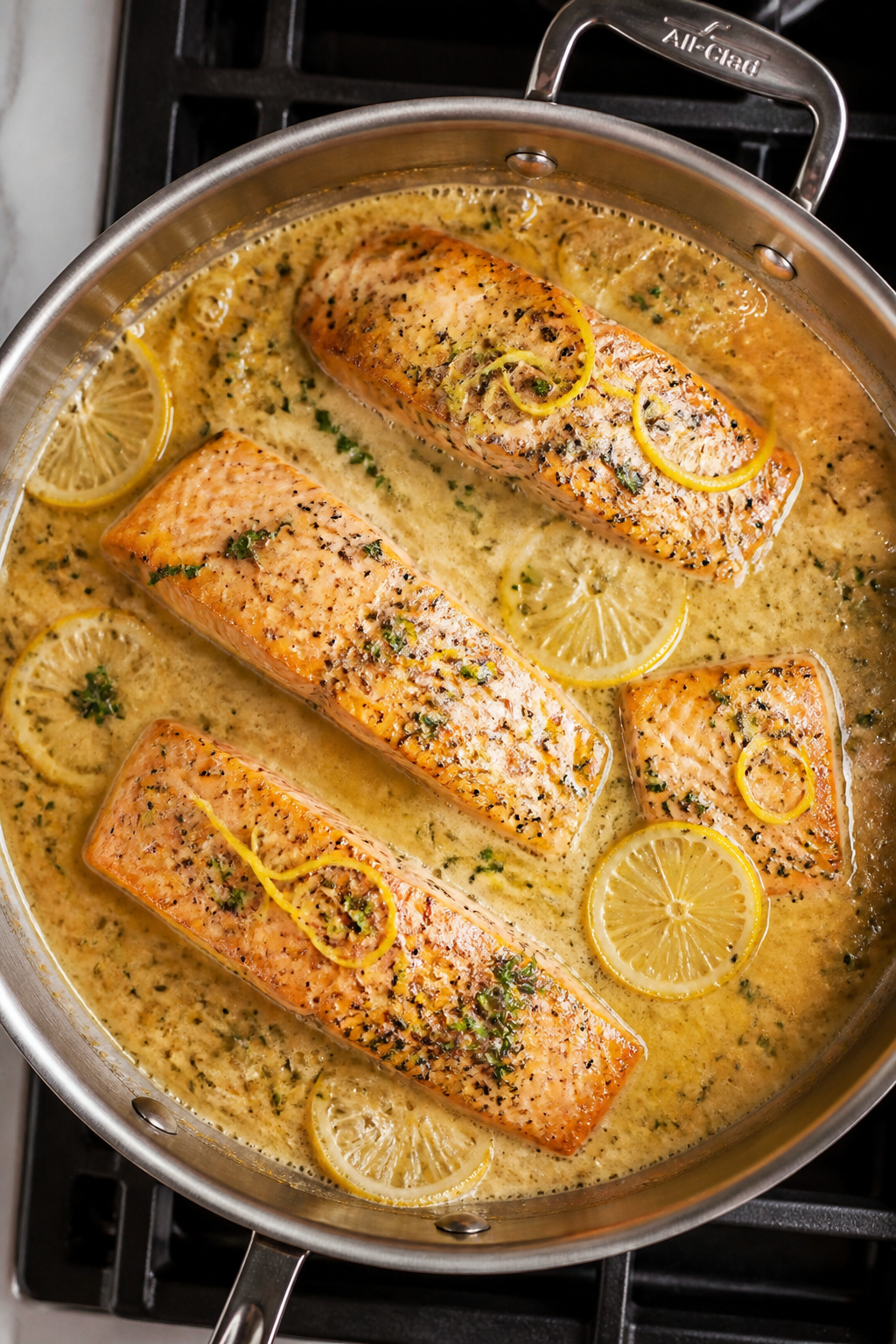 Cooking process: Overhead shot of salmon portions nestled in a bubbling garlic butter cream sauce in