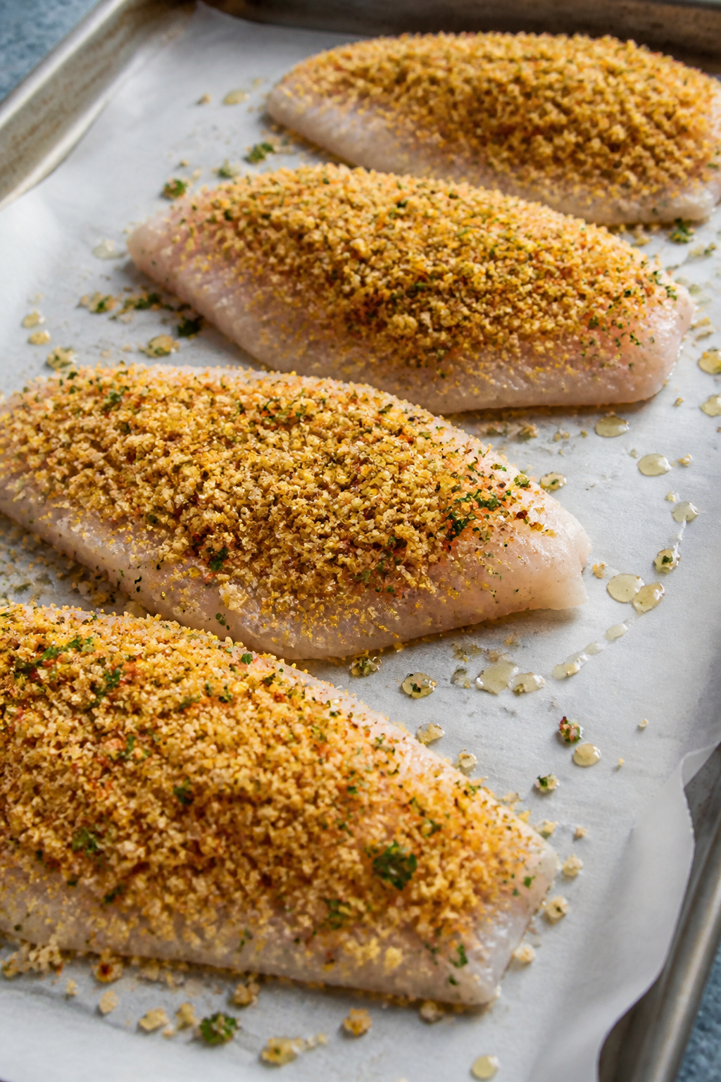 Cooking process: Tilapia fillets on a lightly oiled parchment-lined sheet pan being topped with the 