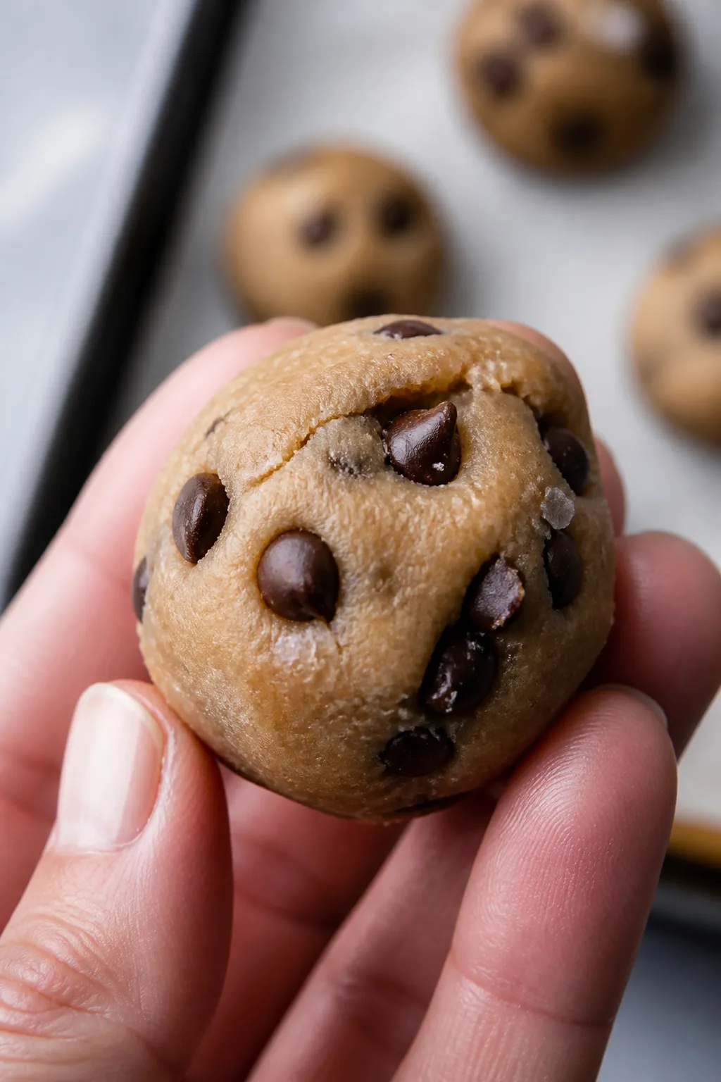 Close-up detail: A chilled ball of Low Carb Protein Cookie Dough Bite midway through rolling, glossy
