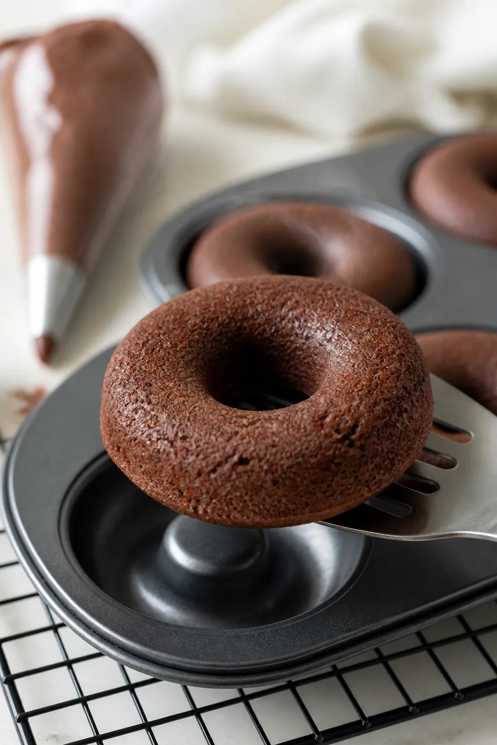 Close-up detail: A just-baked chocolate protein donut being lifted from a nonstick donut pan onto a 