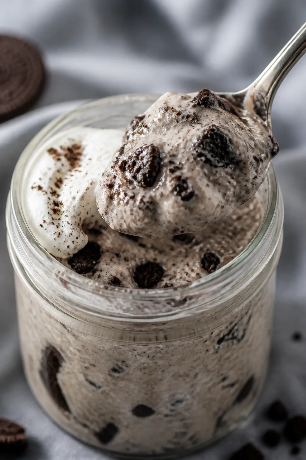 Close-up detail: A spoonful of cookies-and-cream protein pudding lifted from a chilled glass jar, sh