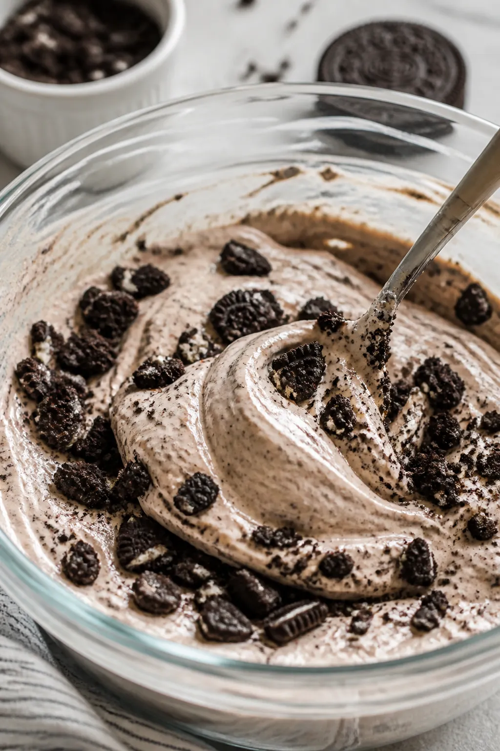 Close-up detail: Creamy high-protein Oreo pudding being folded with crushed Oreo pieces in a glass m