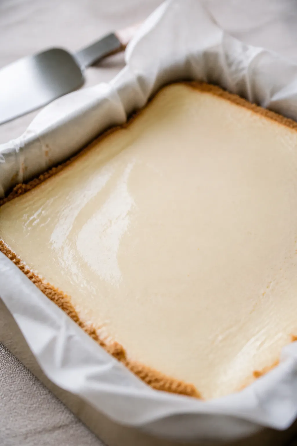 Close-up detail: Freshly baked vanilla protein cheesecake slab cooling in the parchment-lined 8x8 pa