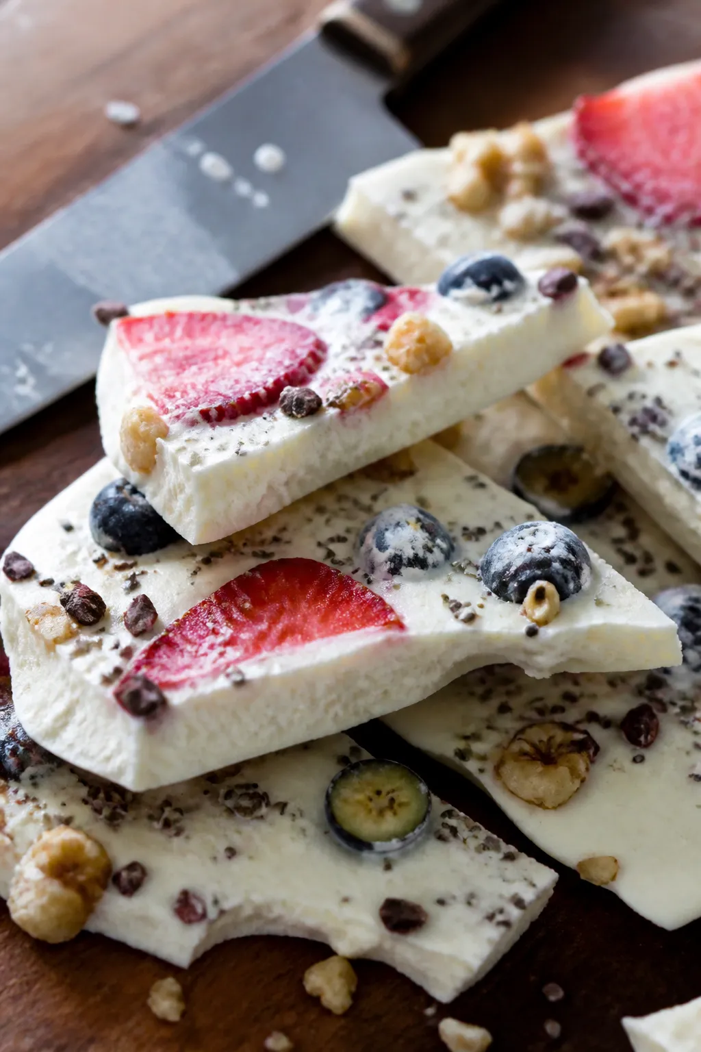 Close-up detail of yogurt bark shards just after breaking on a wooden cutting board, highlighting th
