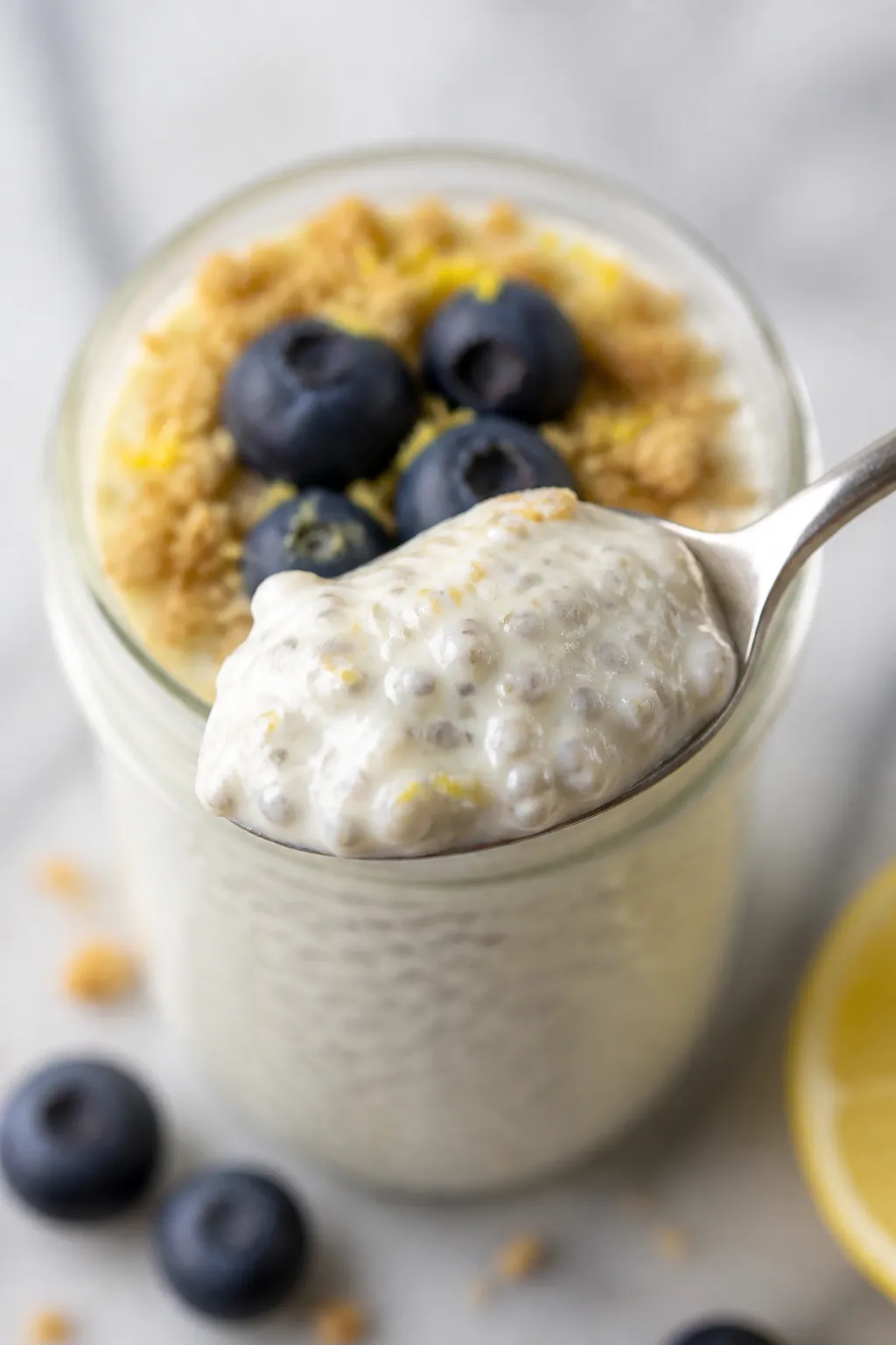 Close-up detail shot: A spoonful of lemon cheesecake chia pudding lifted from a chilled glass jar, s