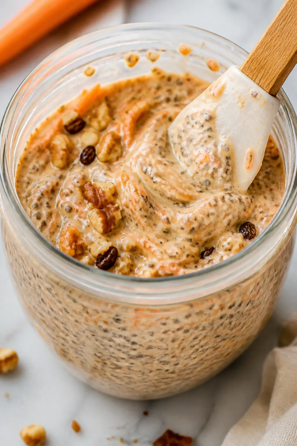 Close-up detail shot: Creamy carrot cake chia pudding mid-thicken in a clear glass jar after the fir