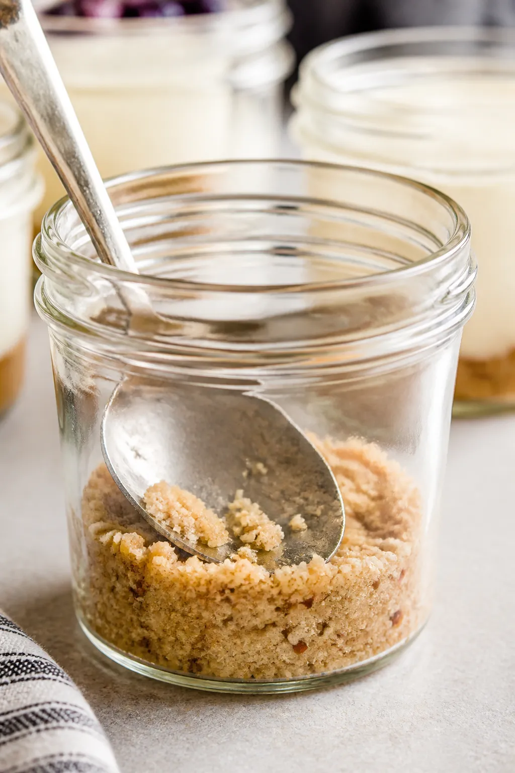 Close-up detail shot of a prepared cheesecake jar as the almond flour “crust” is being lightly p