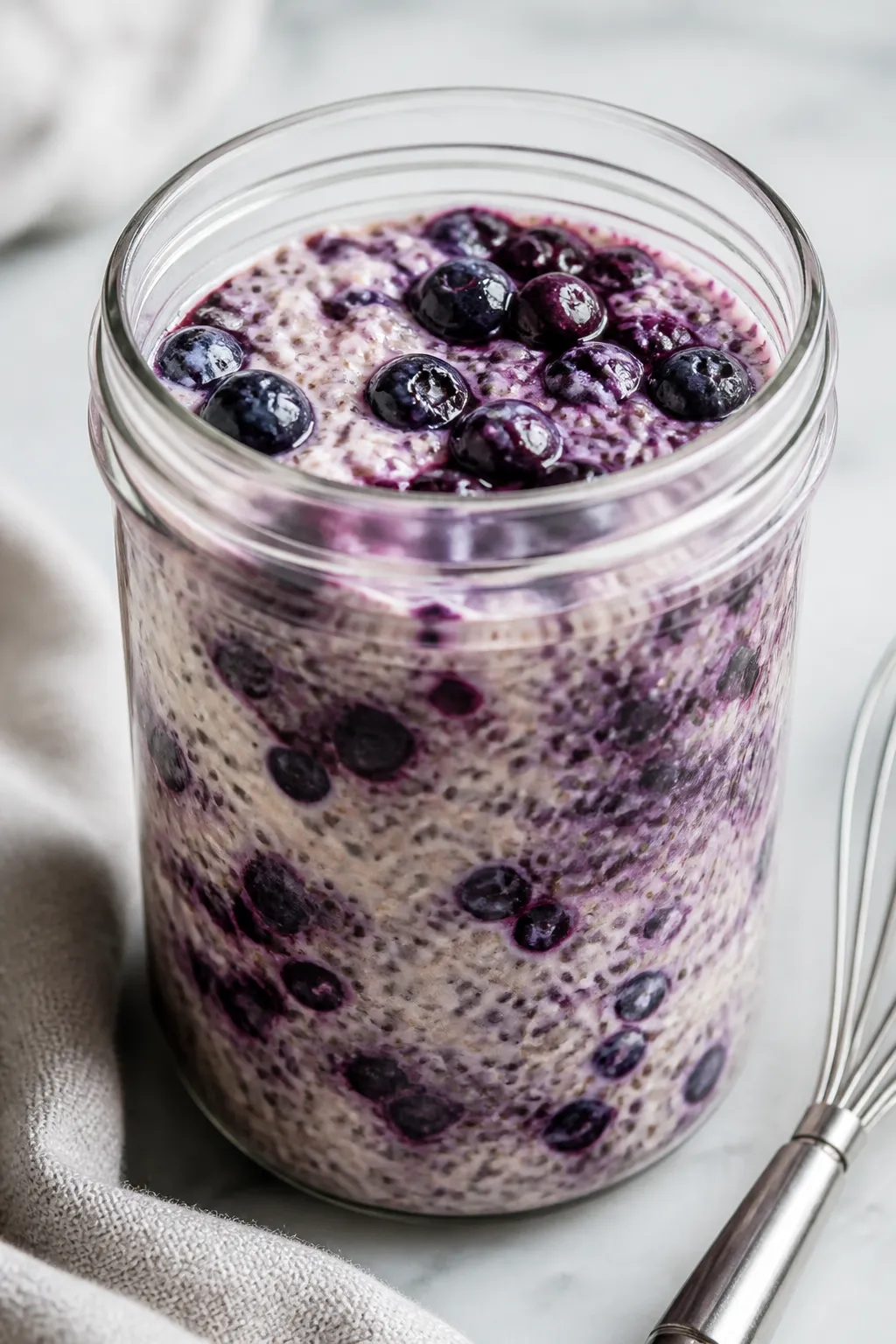 Close-up detail shot: Thick, creamy blueberry muffin chia pudding mid-set in a clear glass jar after