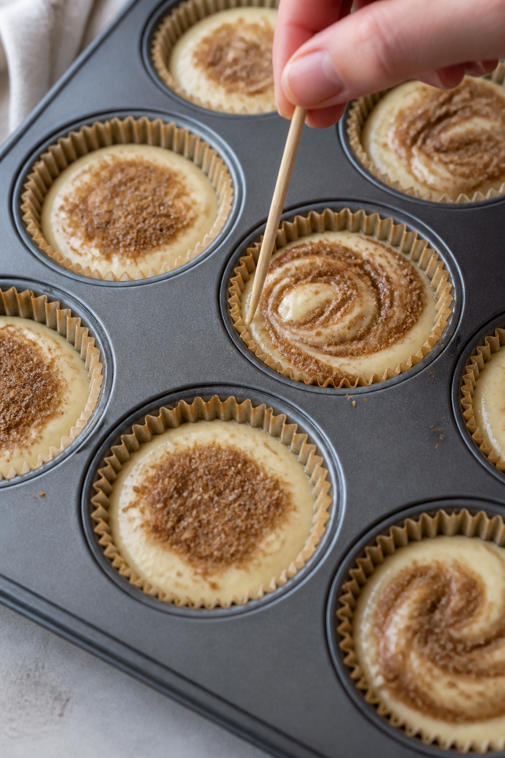 Cooking process: Action shot of the layering and swirling step—muffin cups filled about halfway wi