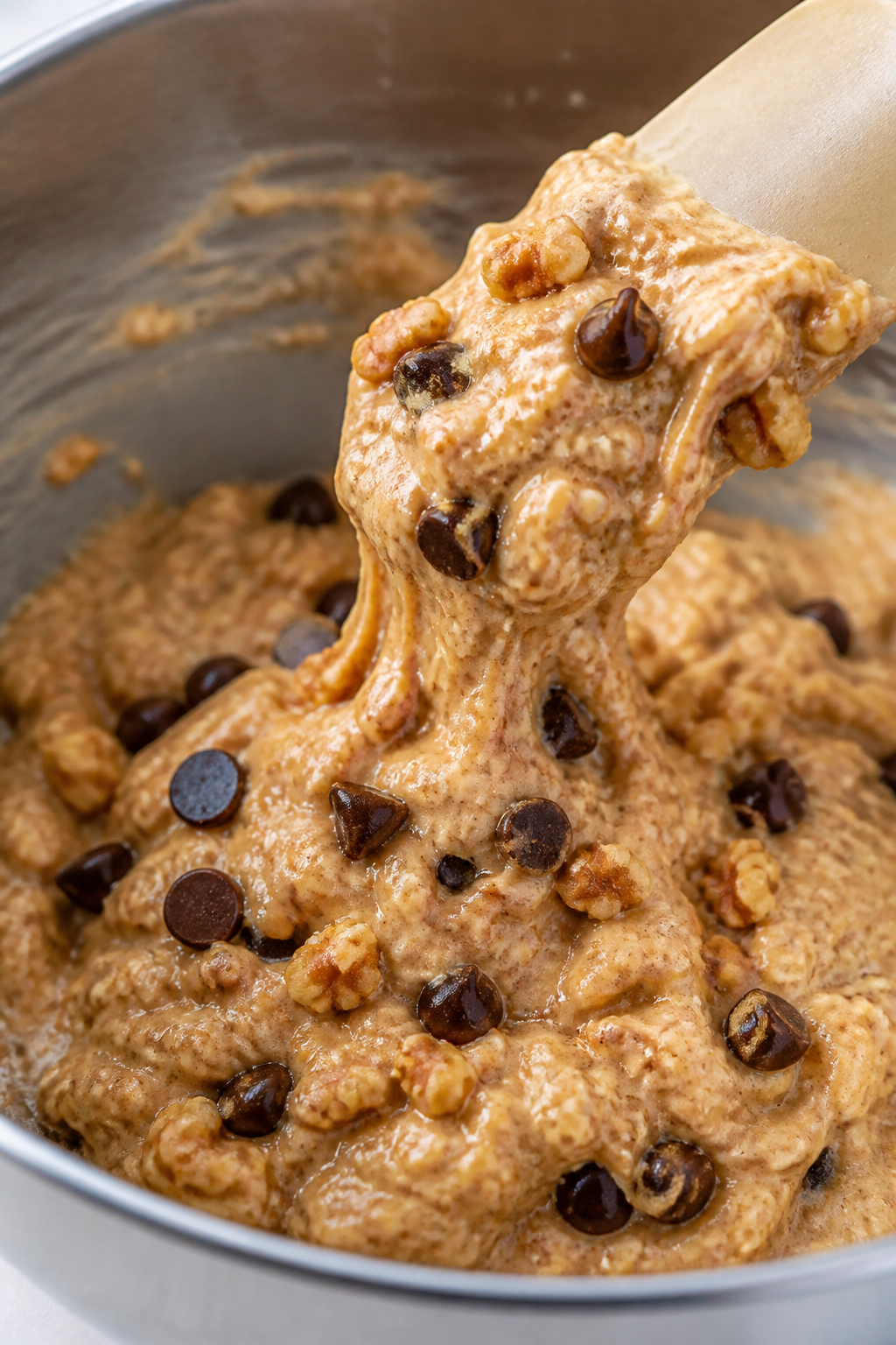 Cooking process close-up: Thick banana-oat-protein muffin batter being gently folded with dark choco