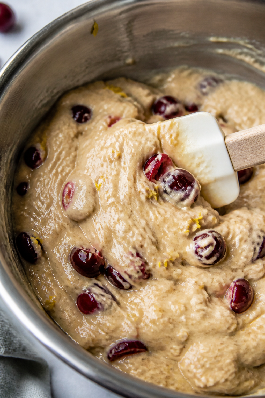 Cooking process close-up: Thick muffin batter being gently folded with ruby-red cherry pieces visibl