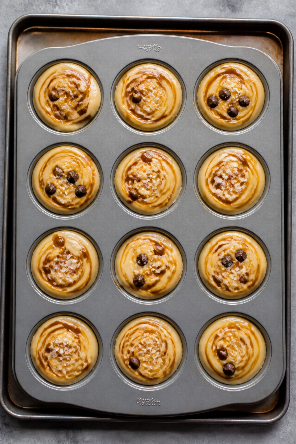 Cooking process: Overhead shot of a 12-cup muffin tin just after the caramel swirl step—each muffi