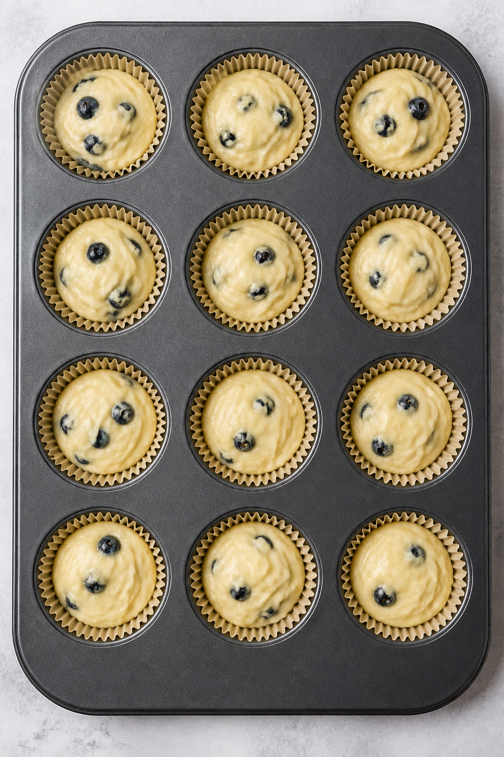 Cooking process: overhead shot of muffin batter being portioned into a lined 12-cup muffin tray, bat
