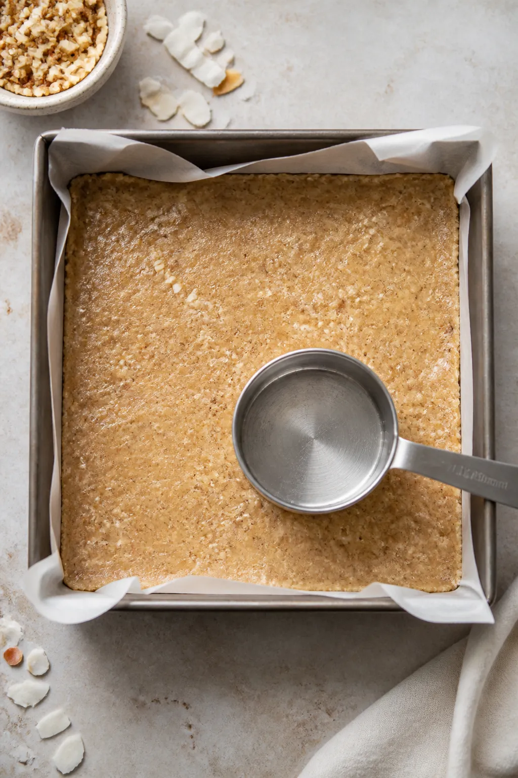 Cooking process shot: Overhead view of the mixture being firmly pressed into a parchment-lined 8x8-i