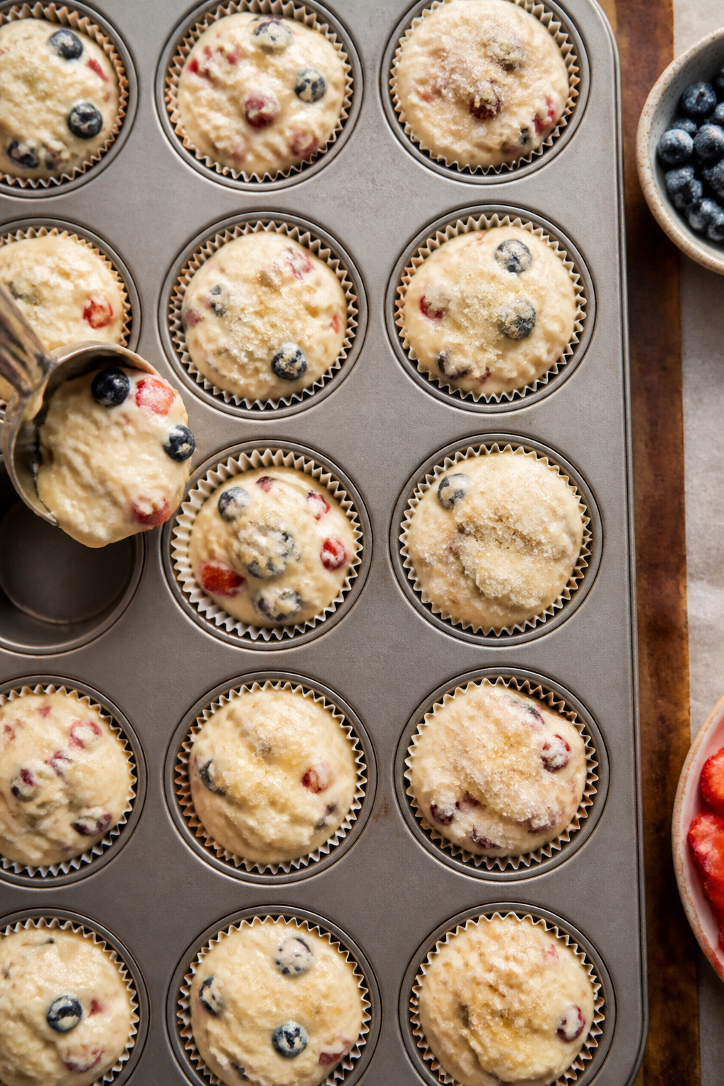 Cooking process shot: thick, scoopable batter being portioned to the brim of a lined muffin tin at 3