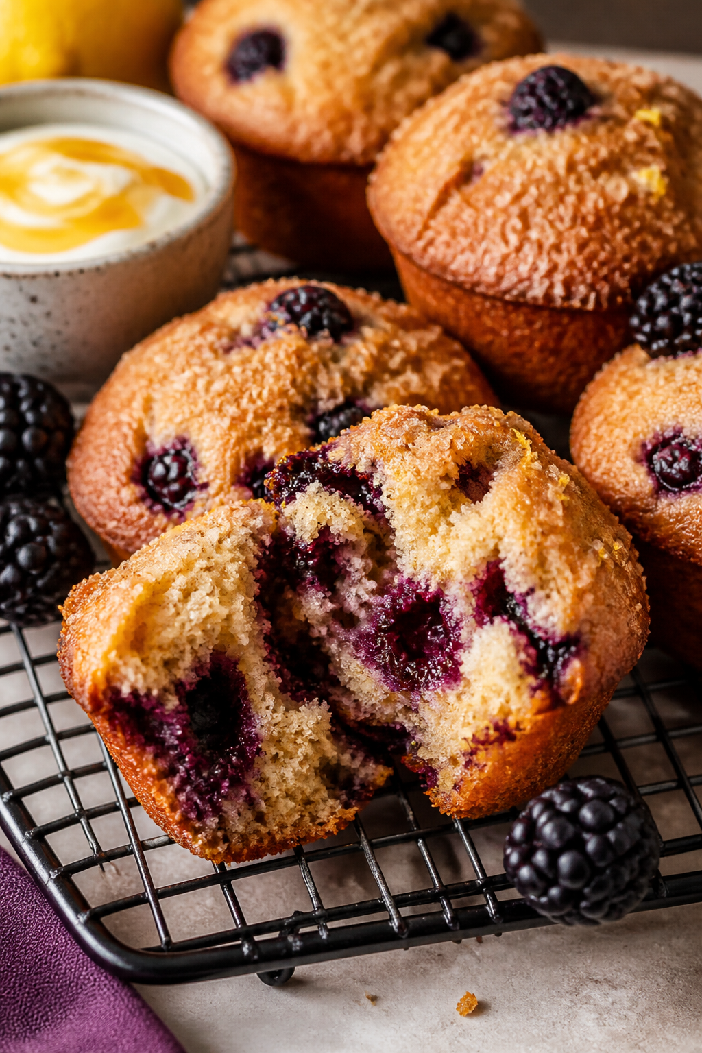 Final dish presentation, close-up: Warm blackberry protein muffins on a wire rack, one muffin torn o
