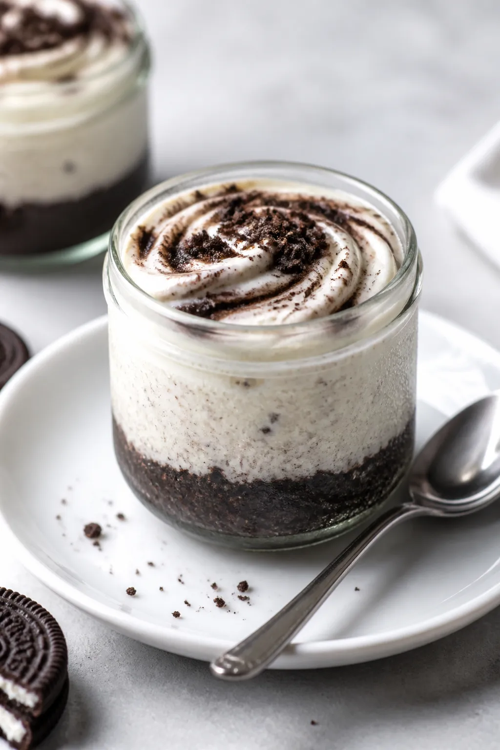 Final plated hero shot: a single Oreo cheesecake jar presented on a white ceramic saucer with a smal