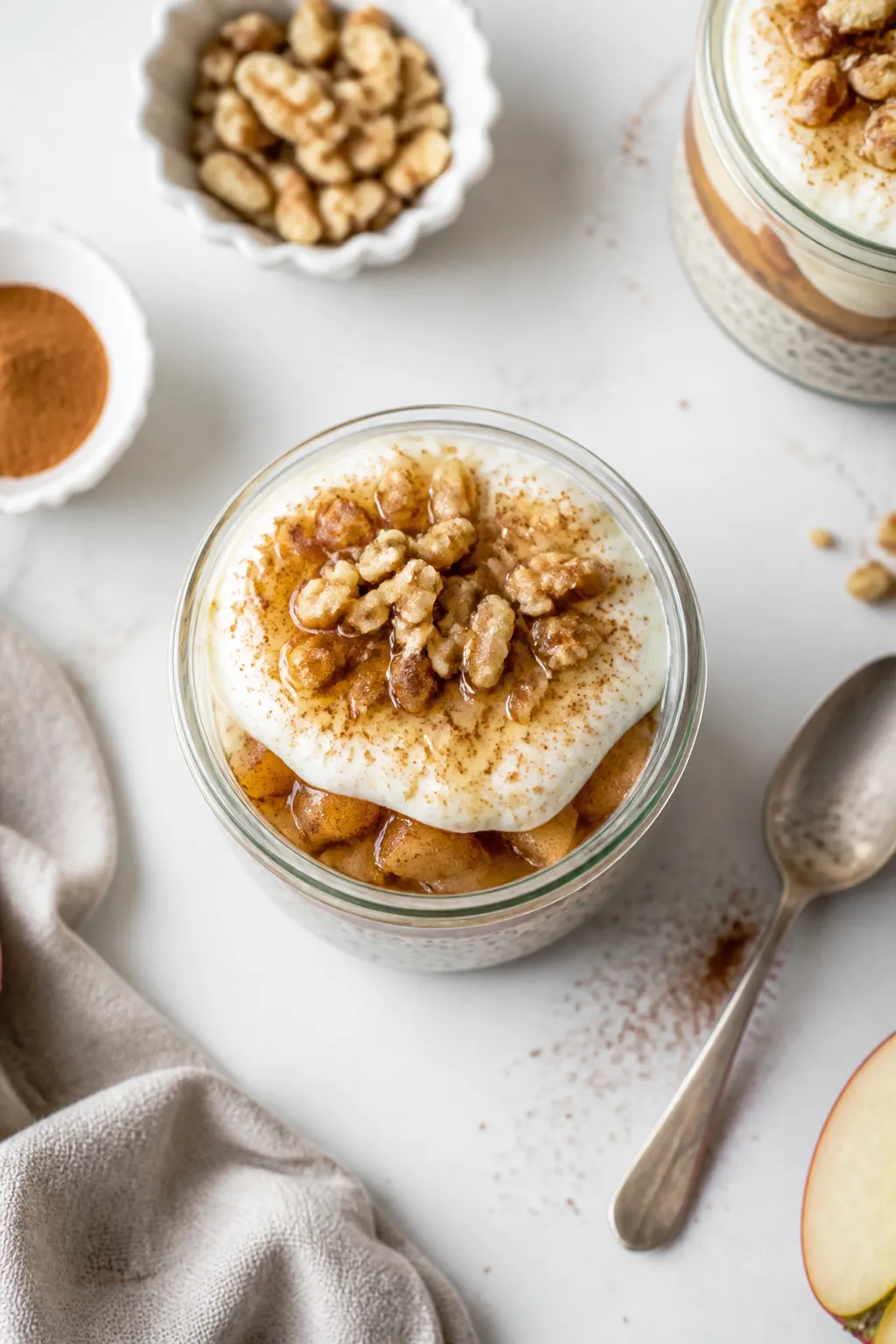 Overhead “assembly” shot: Thick, creamy apple pie chia pudding layered in a clear glass jar—vi