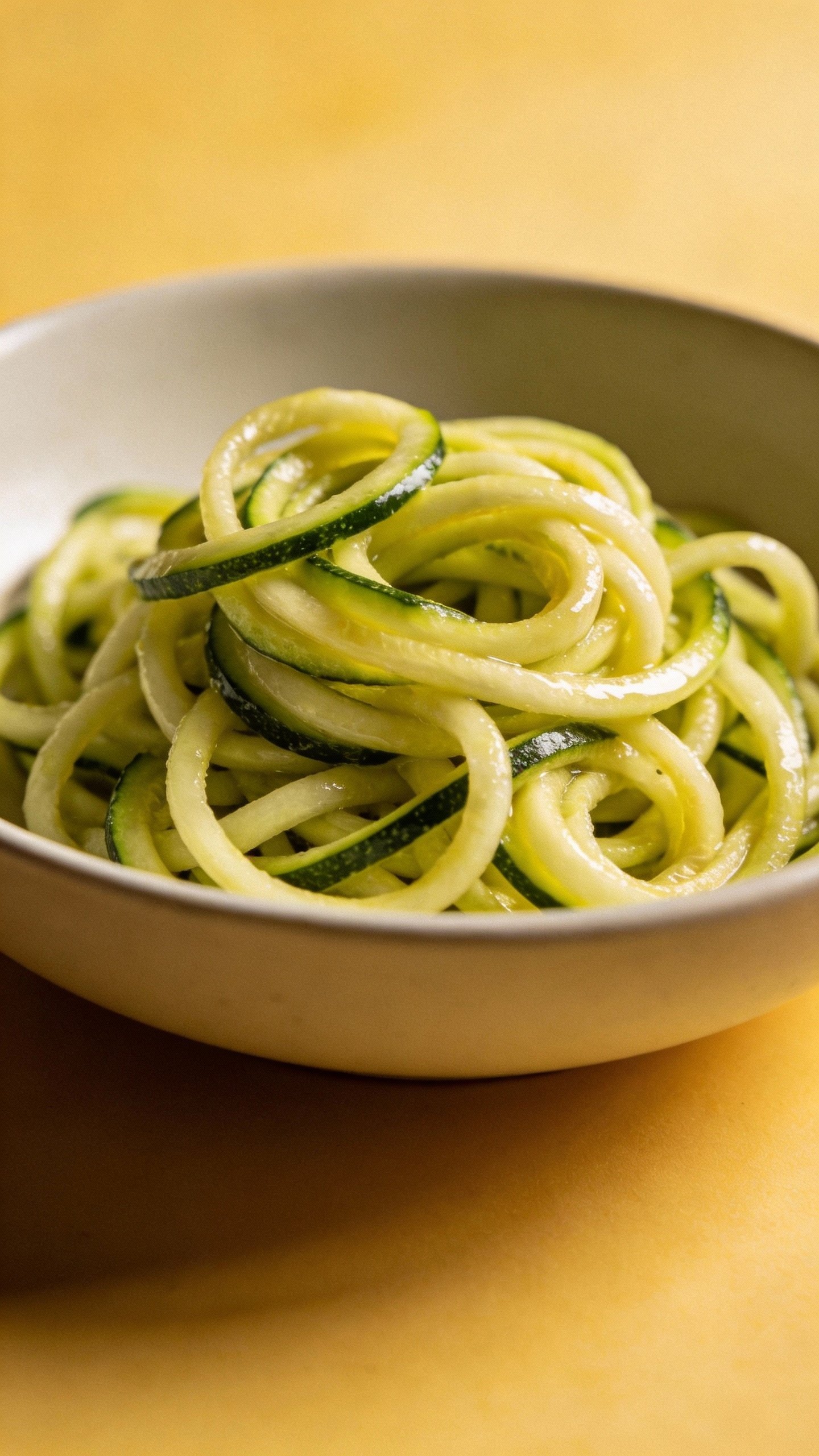 twirled zucchini noodles in shallow white bowl, glossy