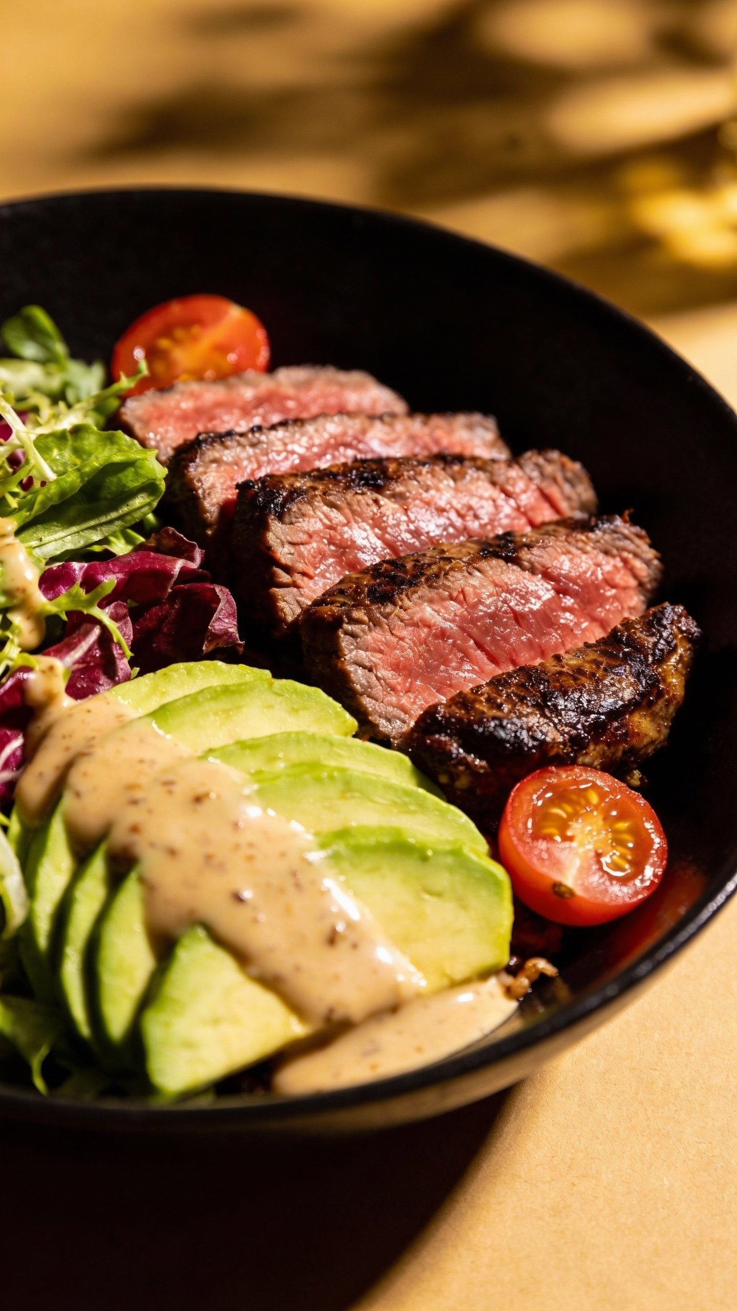 closeup steak and avocado bowl on matte black plate
