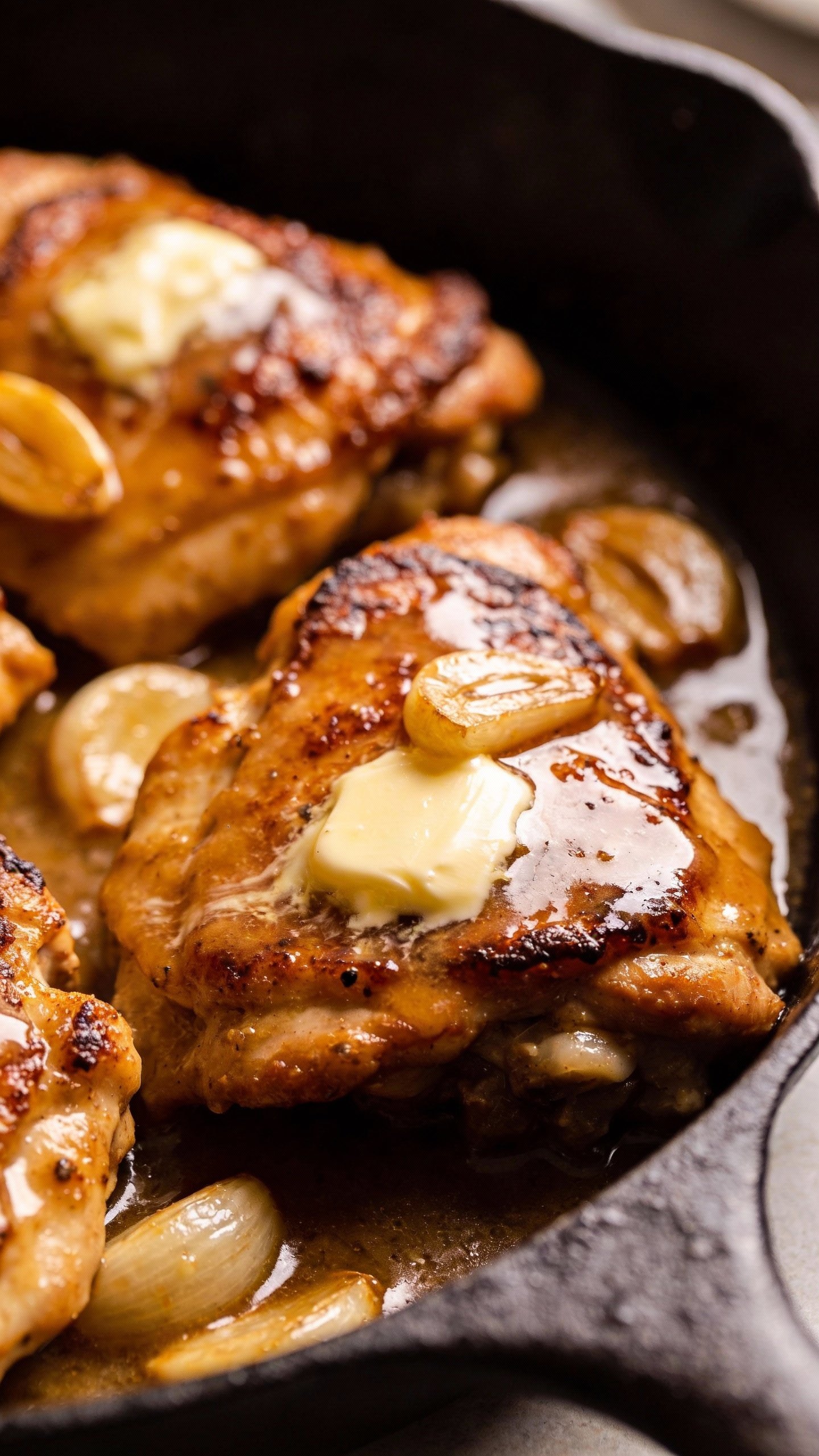 closeup skillet of garlic butter chicken thighs, glossy sauce