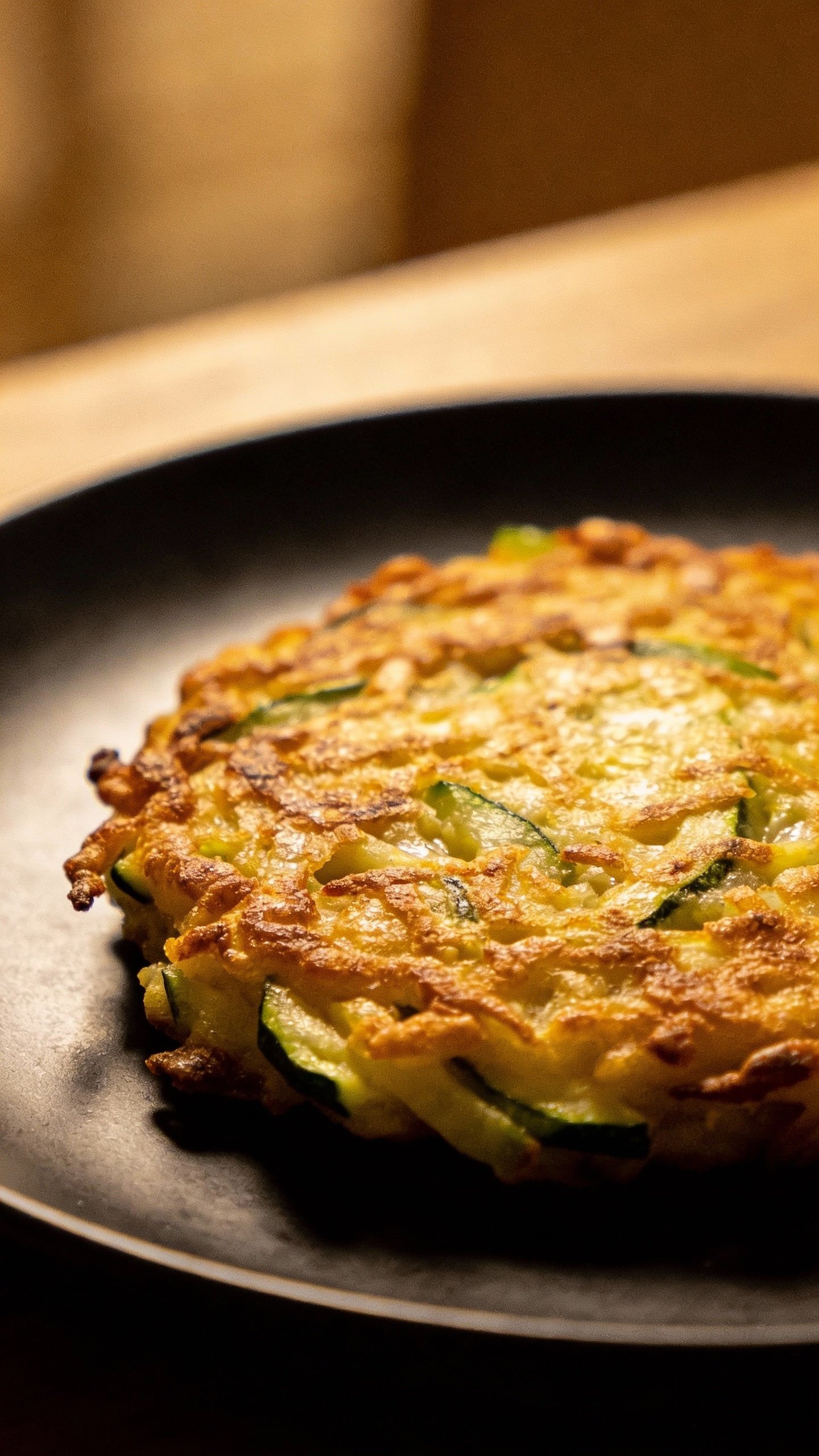 closeup of golden zucchini fritter on matte black plate