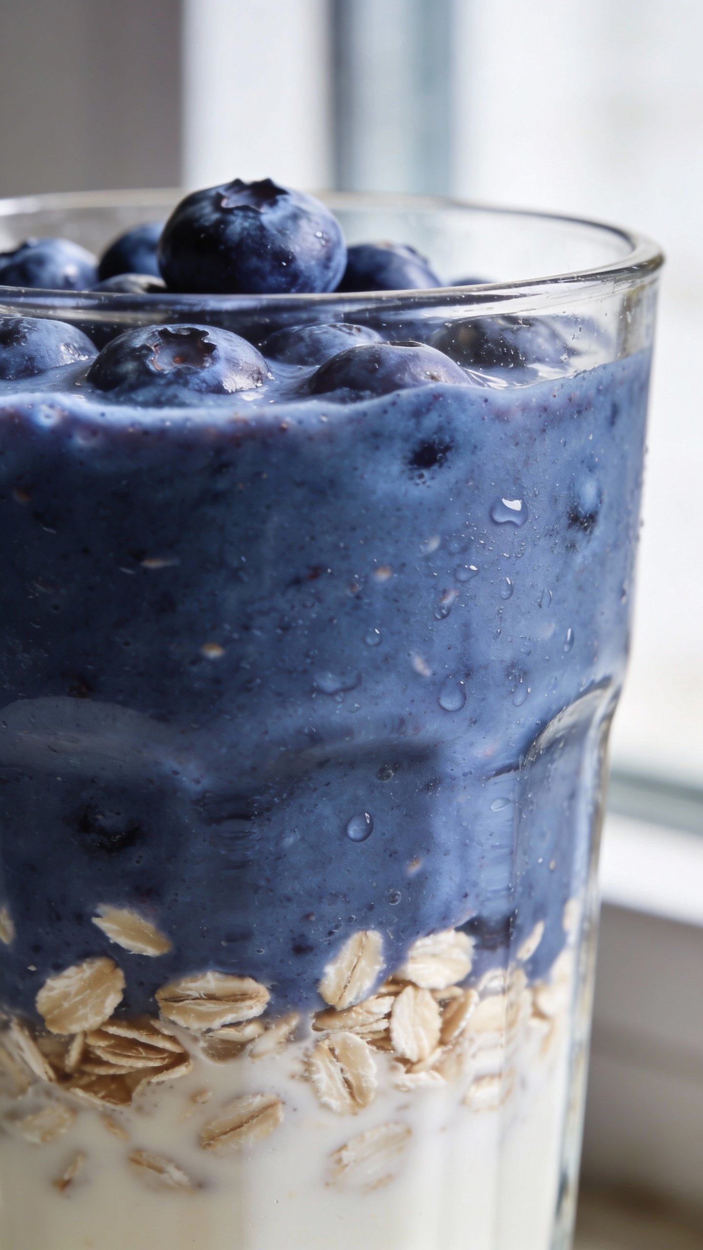 closeup blueberry oat smoothie in clear glass, soft window light