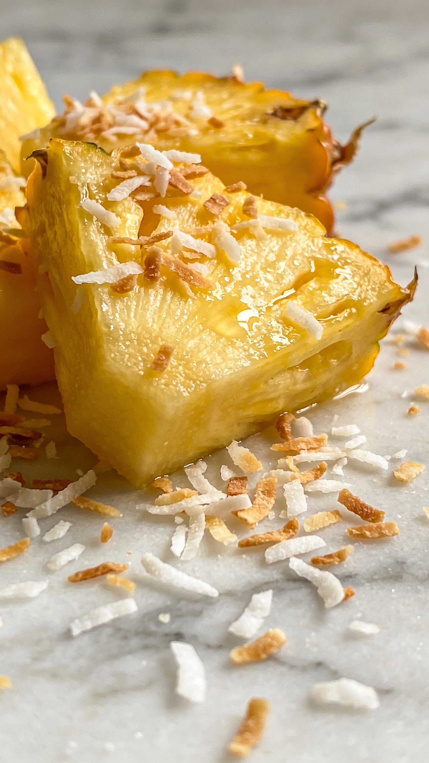 macro shot of fresh pineapple chunks with coconut flakes on marble