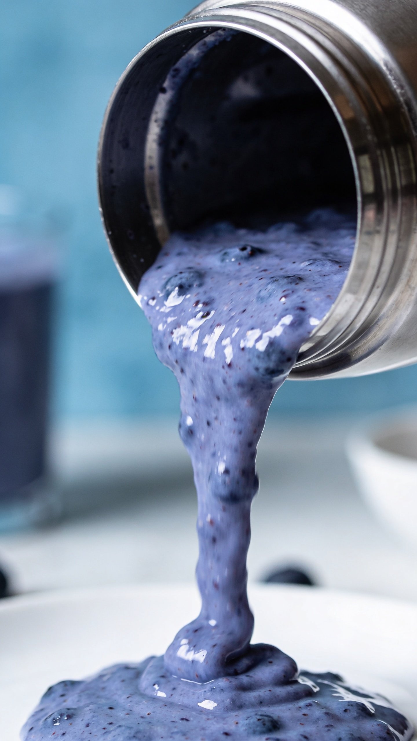 stainless blender jar pouring blueberry smoothie stream, shallow depth