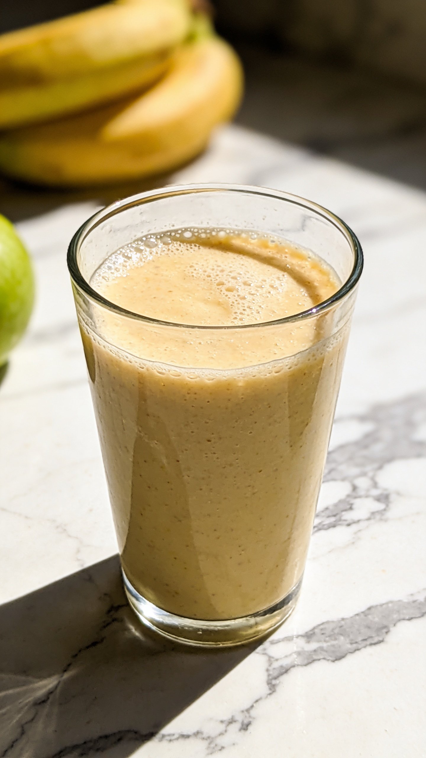 tall glass of apple banana smoothie on marble countertop
