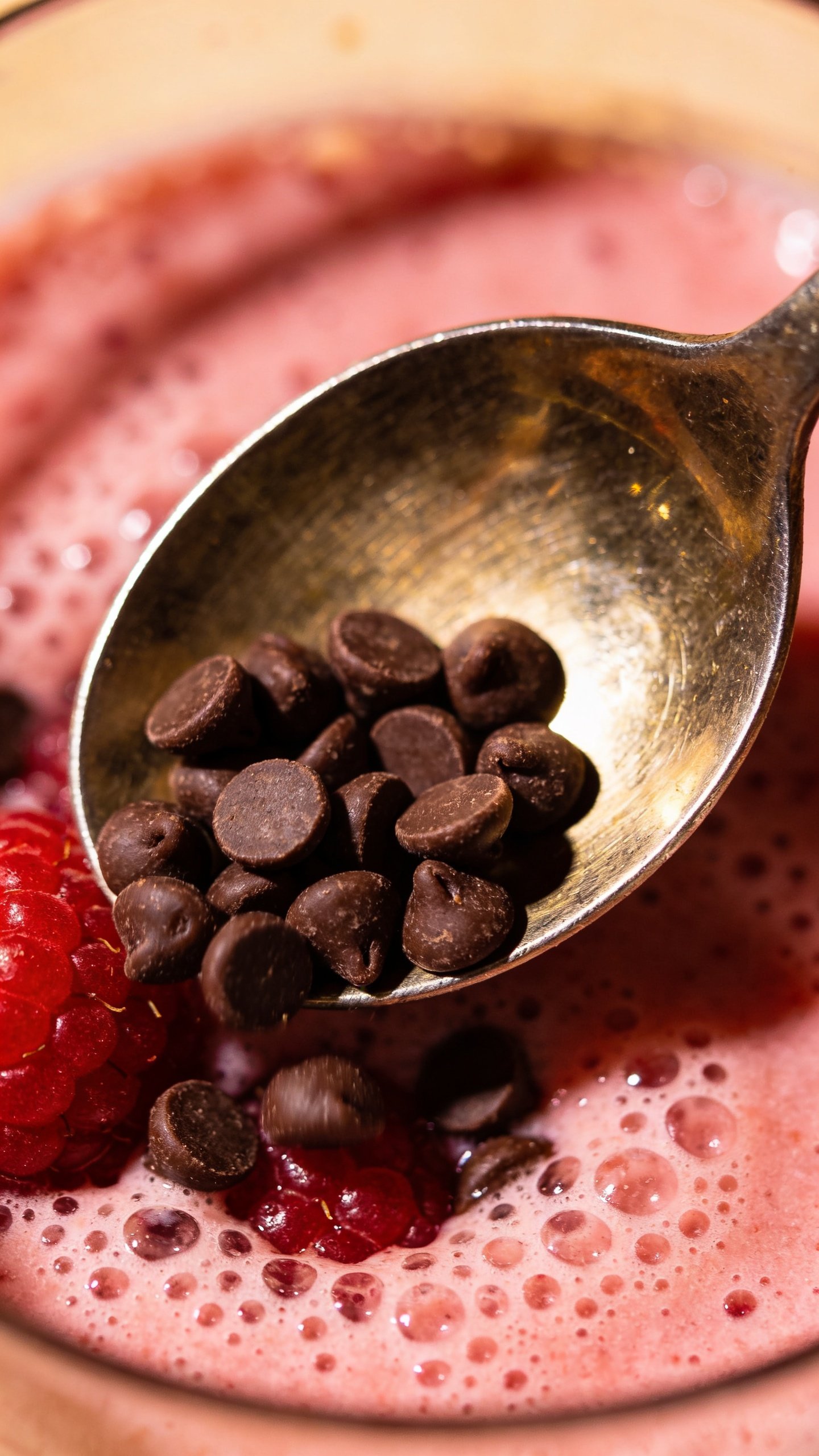 metal spoon scooping chocolate chips over raspberry smoothie, macro