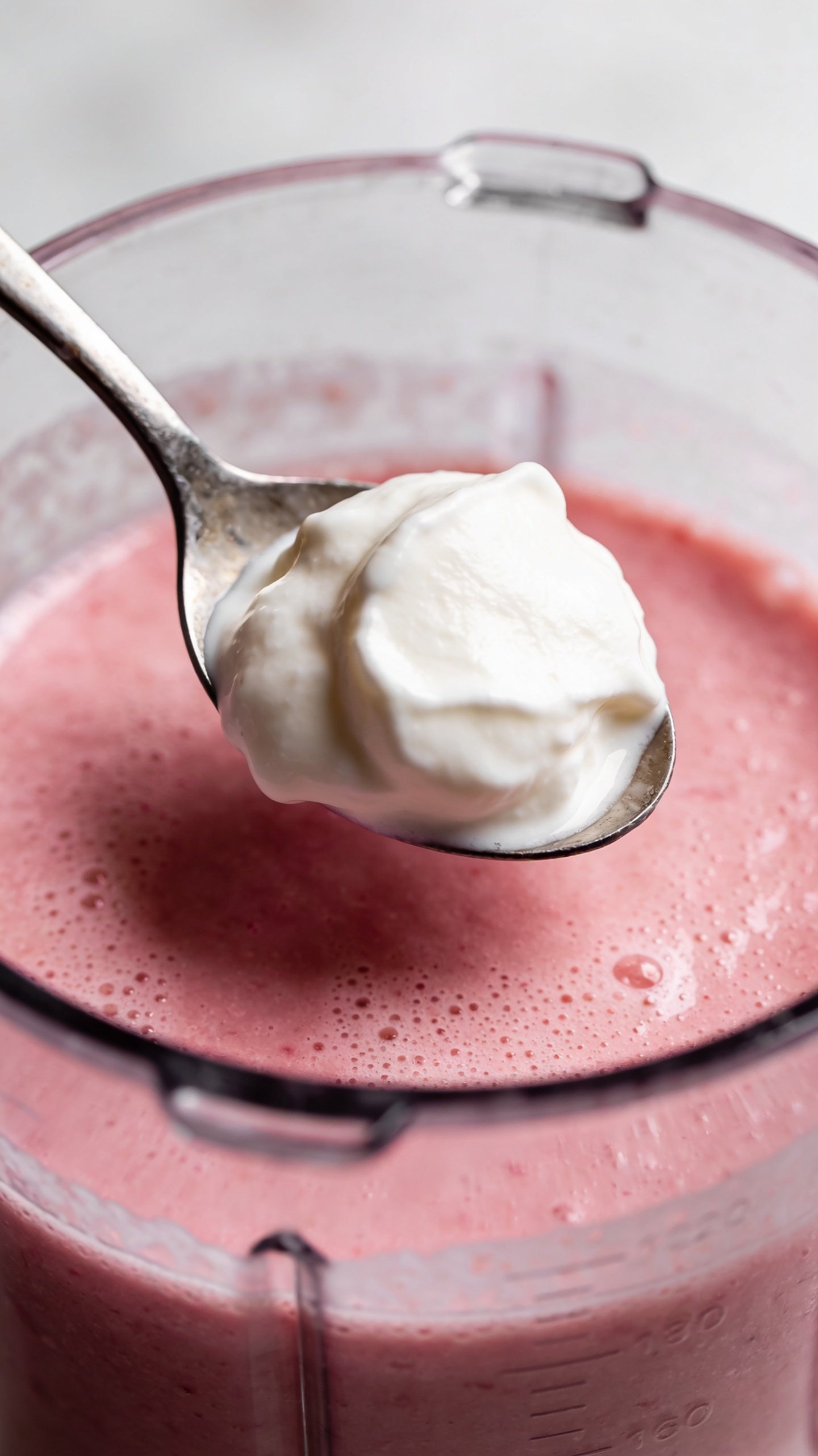 Greek yogurt dollop on spoon above blender of pink smoothie