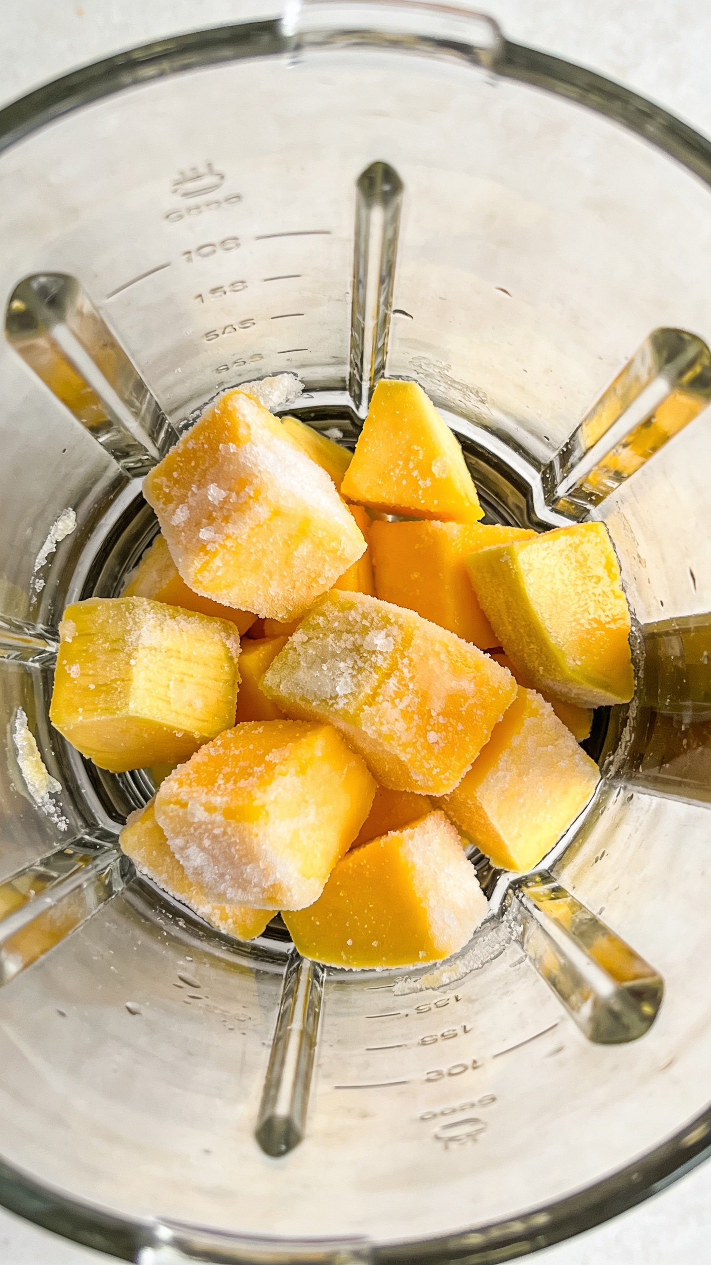 frozen mango chunks in blender jar, top-down closeup