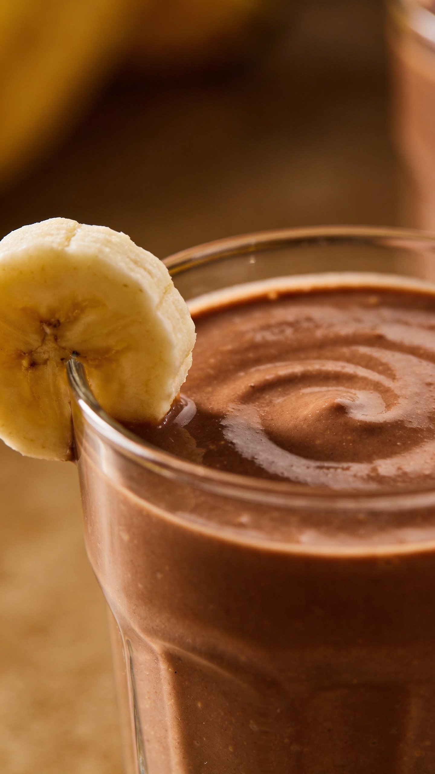closeup chocolate peanut butter smoothie in clear glass, banana garnish
