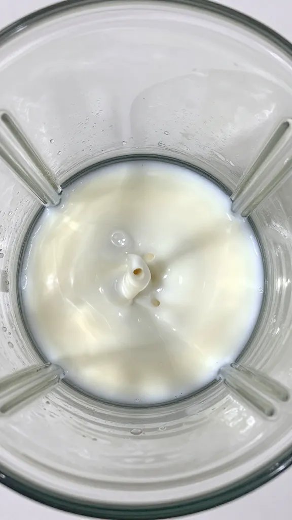 top-down shot of coconut milk pour into blender jar